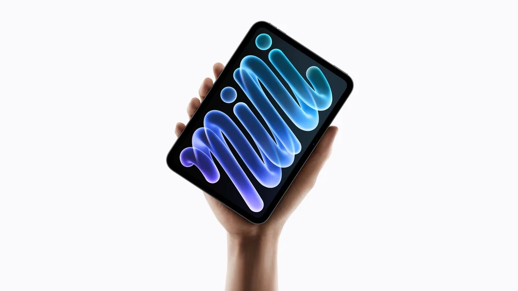 A hand holding up the new iPad mini, its OLED screen showing the word mini in glowing blue and purple script